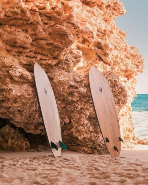 Three Varuna surfboards standing against a rock next to ocean. Varuna surfboards are some of the best wooden surfboards available